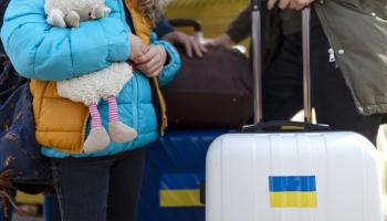 Bilde av barn med bamse og kofferter med ukrainske flagg.