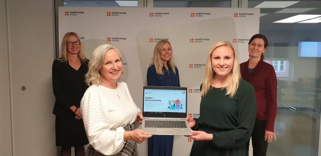 Fem kvinner samlet rundt en bærbar pc.