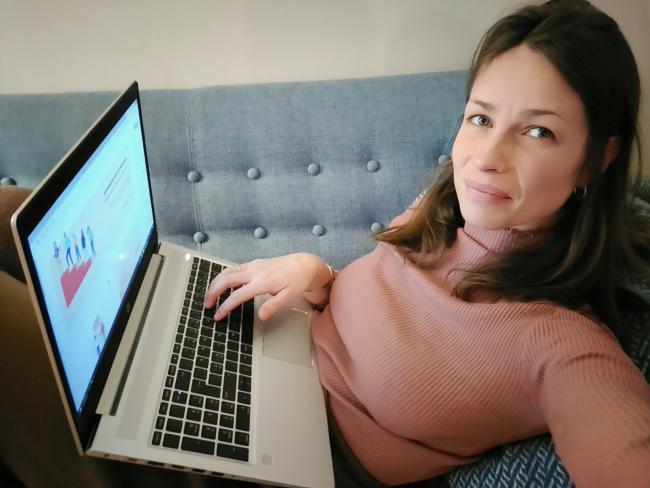 Kvinne ligger på sofa med pc på fanget. 