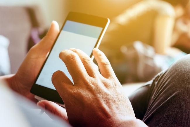 Bilde av en mobiltelefon der man ser kun hendene som taster på mobilen