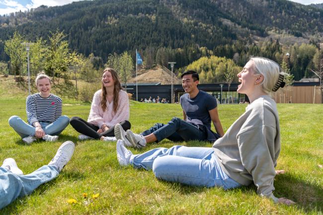 Bilde viser studenter som sitter i ring på en gressplen og prater og ler