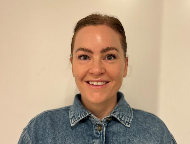 Bilde av smilende, mørkhåret ung dame i dongeriskjorte