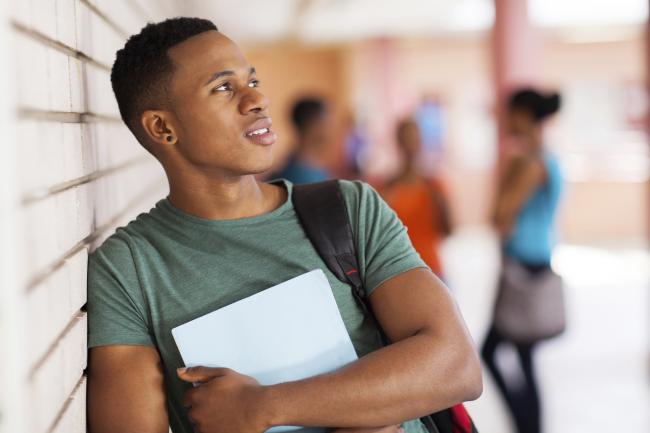 Ung student ser inn i kameraet mens han holder en bunke med papirer.